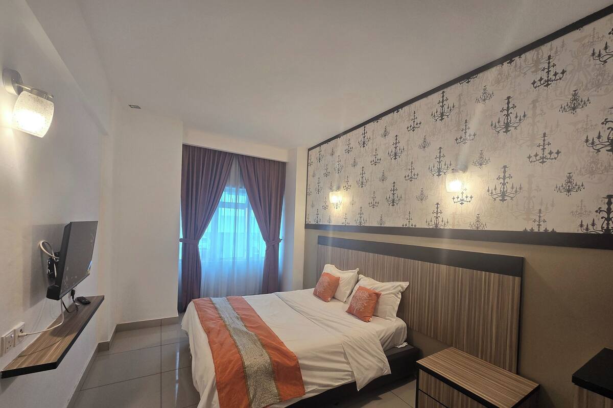 Una habitación de hotel moderna con una cama grande, un escritorio con ordenador y un televisor montado en la pared.