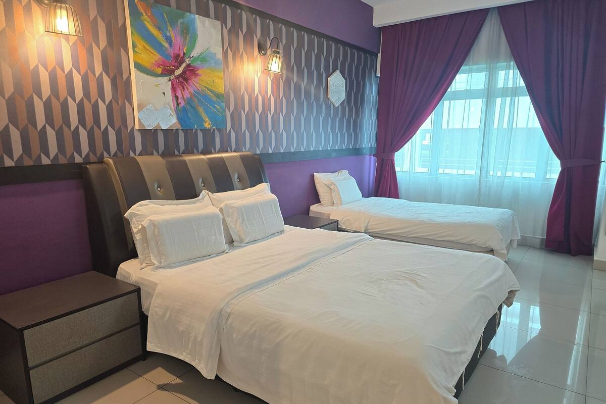Habitación de hotel con dos camas, una mesita de noche, una pared decorativa y una ventana con cortinas.