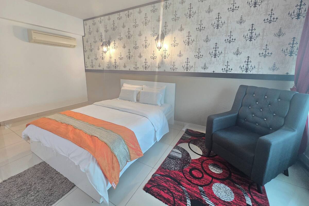 Un dormitorio con una cama, una silla, papel tapiz estampado y un aire acondicionado de pared.