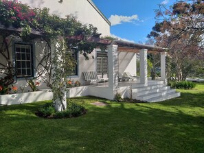 A white house with a covered porch, outdoor seating, and a well-maintained lawn. - L'Auberge Chanteclair (Franschhoek)