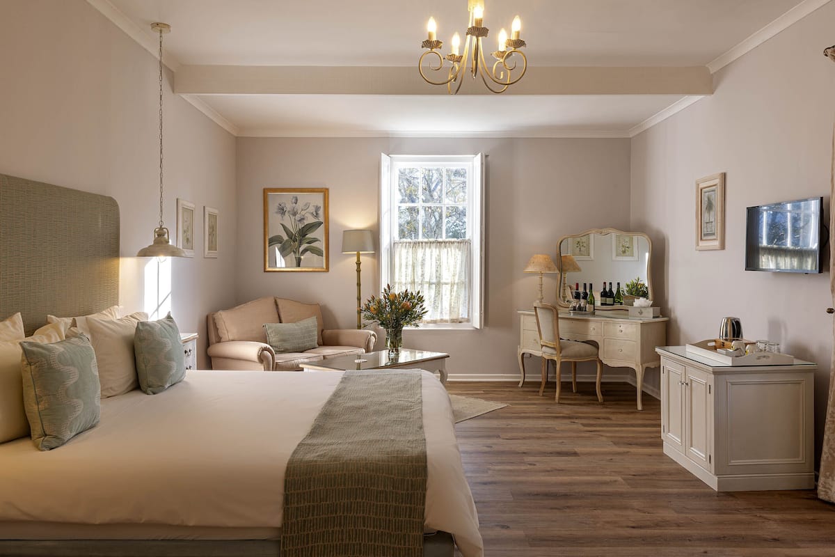 A spacious bedroom with a large bed, a vanity with a mirror, and a desk with a chair.