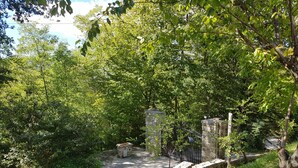 Un sentier qui traverse une zone boisée, bordée de murs de pierre et fermée par un portail en métal.