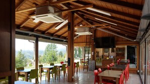 Une salle à manger spacieuse avec des poutres en bois, de grandes fenêtres et une vue sur l’extérieur.