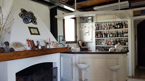Un espace bar avec un comptoir blanc, des étagères remplies de bouteilles, une cheminée et un mur décoratif.