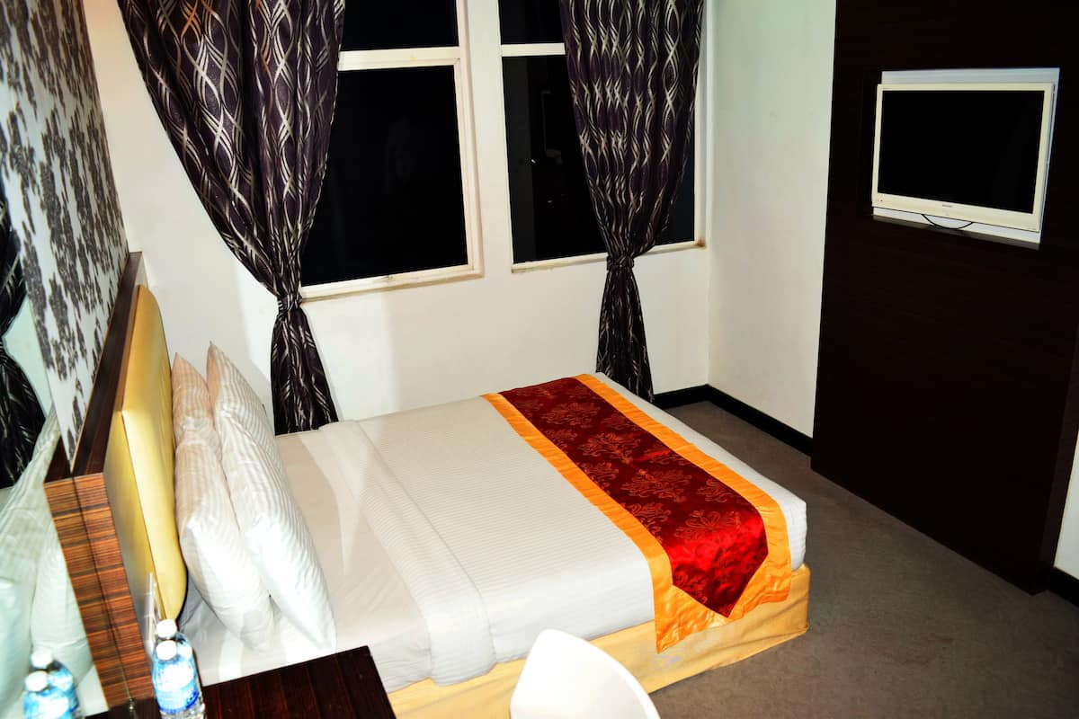 A neatly made bed with a white and red bedspread, a bedside table with a lamp, and a TV mounted on the wall.