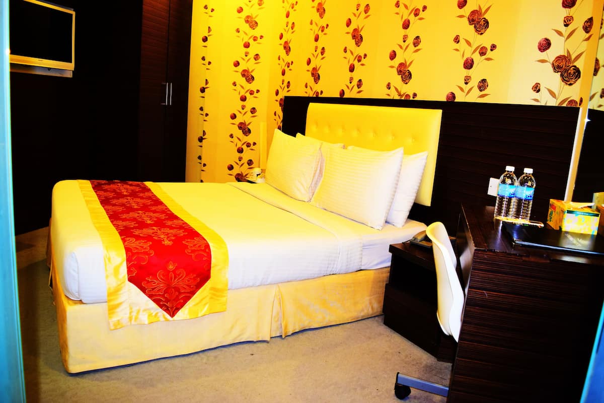 A hotel room with a large bed, a bedside table with a lamp, a chair, and a wall-mounted TV.