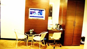 Une chambre d’hôtel avec une armoire en bois, un bureau avec une machine à café, un téléviseur fixé au mur et deux fauteuils en osier.