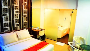 Une chambre d’hôtel comprenant un lit, un bureau avec une chaise, une petite table avec des chaises et une salle de bain visible à travers une porte ouverte.