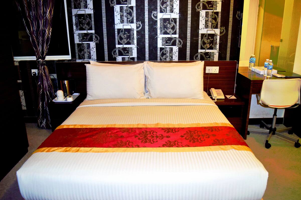 A hotel room with a large bed, a desk with a telephone, and a chair.