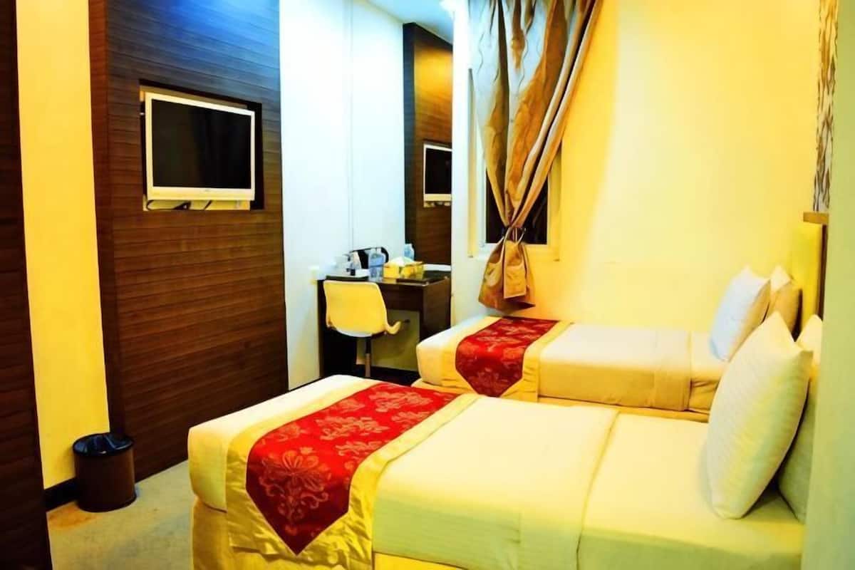 A hotel room with two beds, a desk, a chair, and a television.