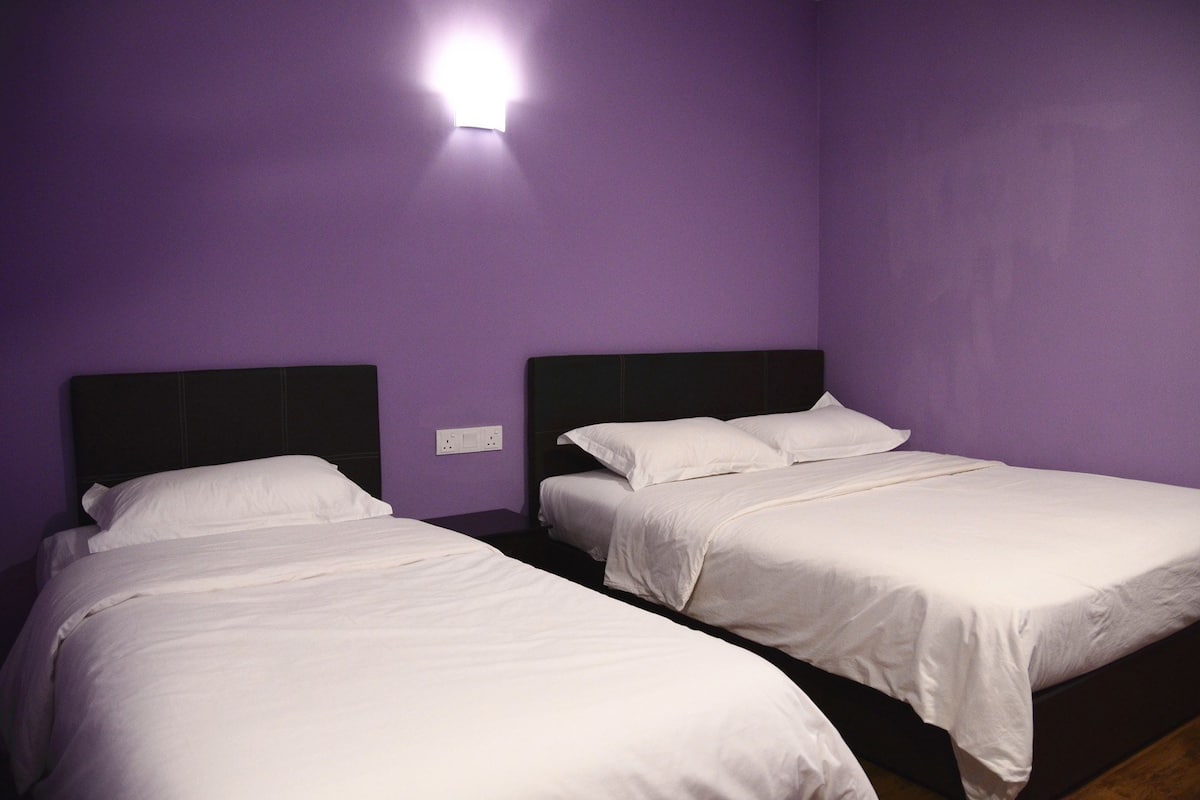 Een kamer met twee éénpersoonsbedden, elk met witte lakens en donkere hoofdeinden, tegen een paarse muur.