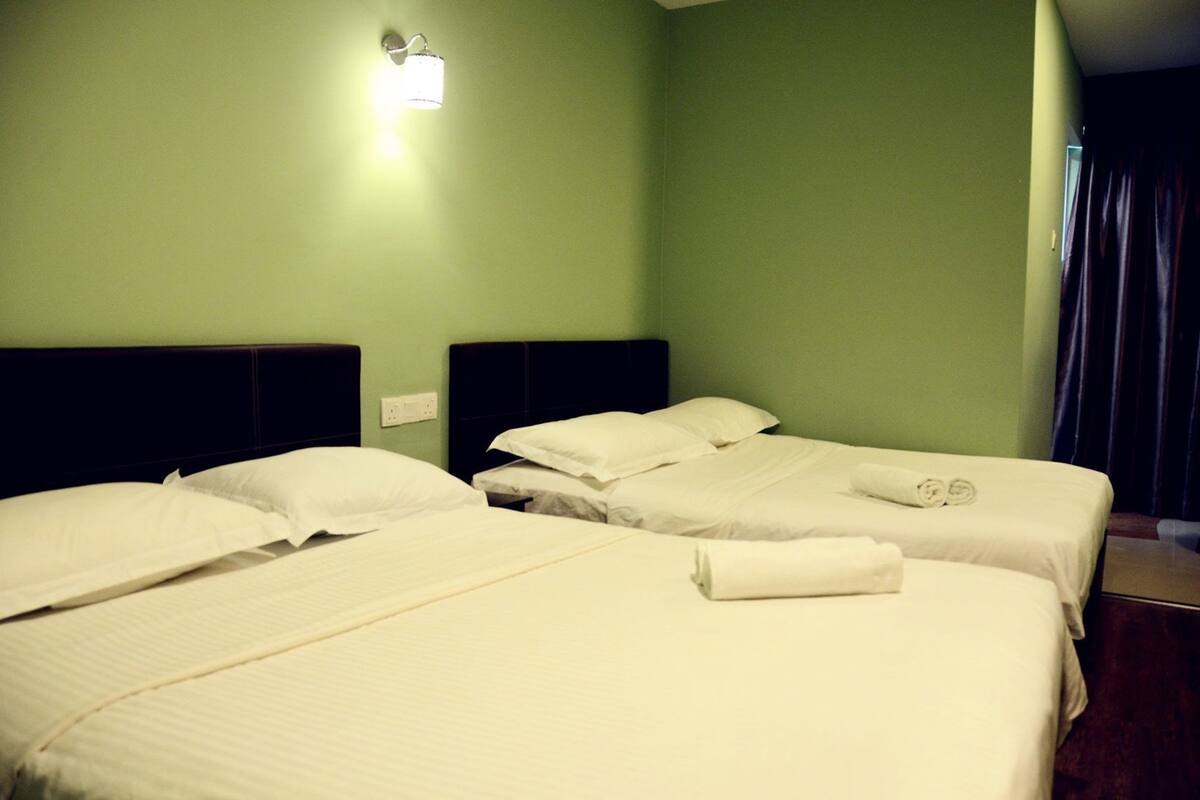 Hotelkamer met twee bedden, elk voorzien van witte lakens en kussens, een nachtkastje, een wandlamp en een gordijn voor het raam.