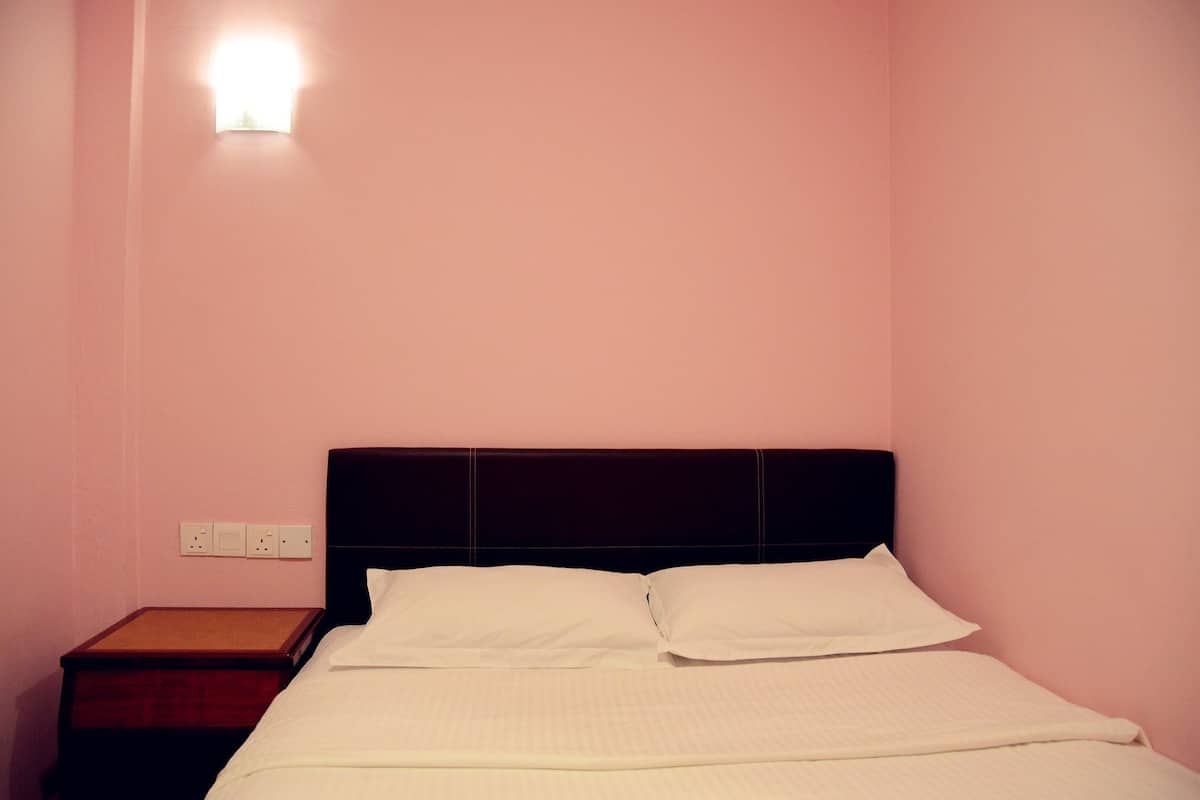 Een enkel bed met een houten hoofdbord in een kamer met roze wanden.