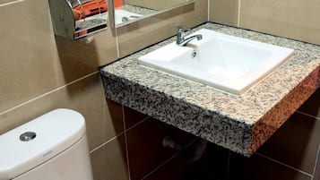 Un baño con inodoro blanco, lavabo con encimera de granito y espejo sobre el lavabo.