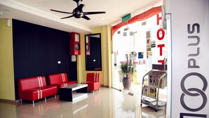 Un hall d’hôtel avec un comptoir d’accueil, un espace détente avec des sièges rouges et un ventilateur de plafond.