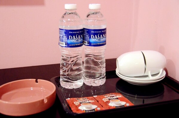 Una bandeja con dos botellas de Dasani, un cenicero blanco, un cenicero rosa y una cajita de mezcla para café.