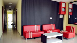 Un hall d’hôtel avec un couloir menant à la sortie, des sièges rouges à rayures blanches et un tableau électrique rouge sur le mur.