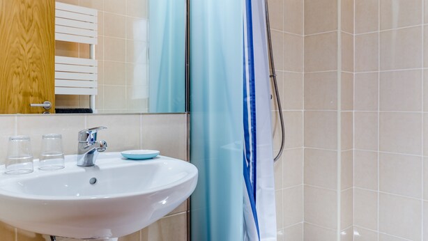 Une salle de bain avec un lavabo blanc, deux verres, un miroir et un rideau de douche.