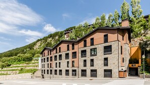 Un immeuble à plusieurs étages, doté d’une façade en pierre et de nombreuses fenêtres, se dressant sur un fond de verdure et sous un ciel dégagé.