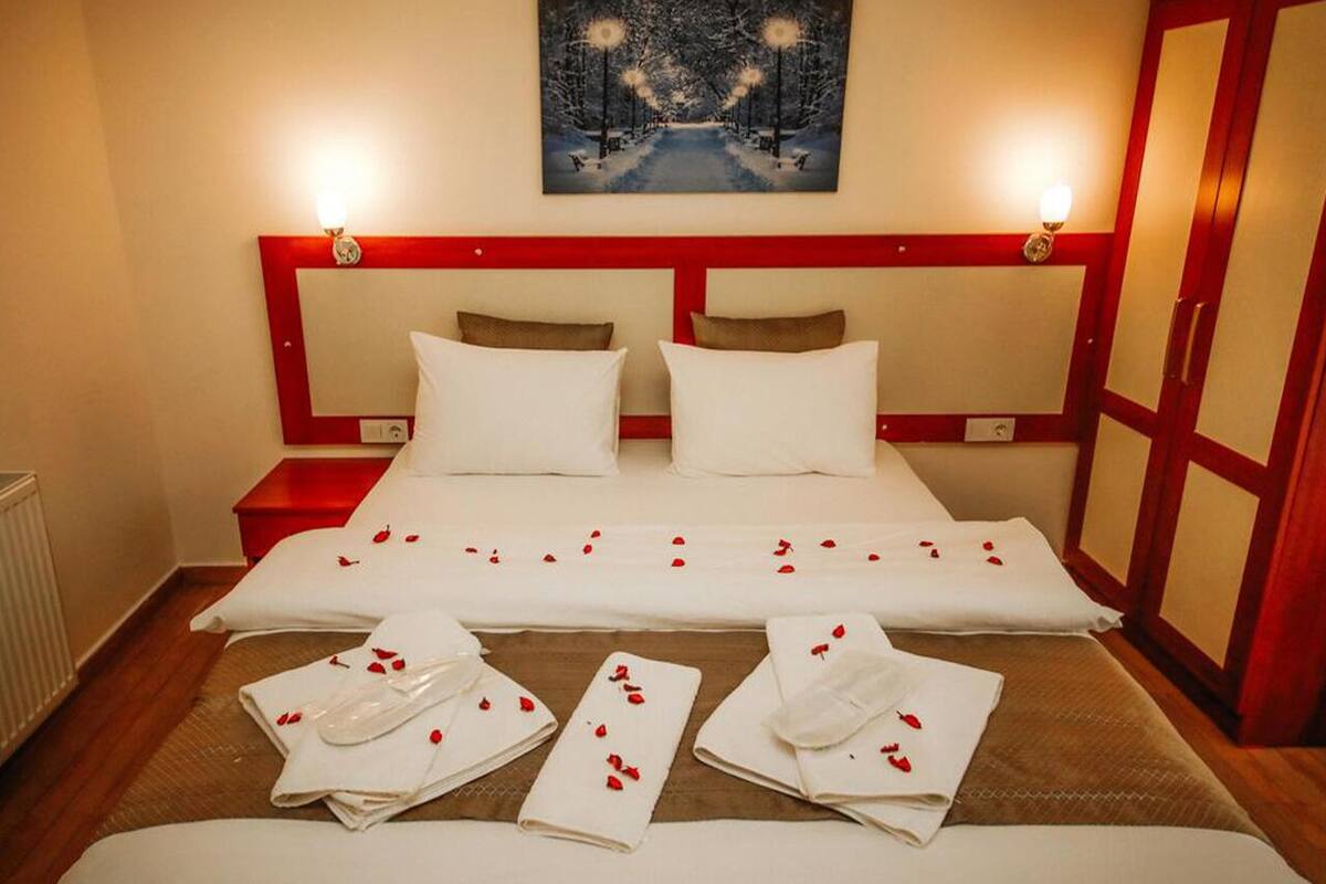 Habitación de hotel con una cama grande, dos mesitas de noche, un cuadro sobre la cama y un armario con marco rojo.