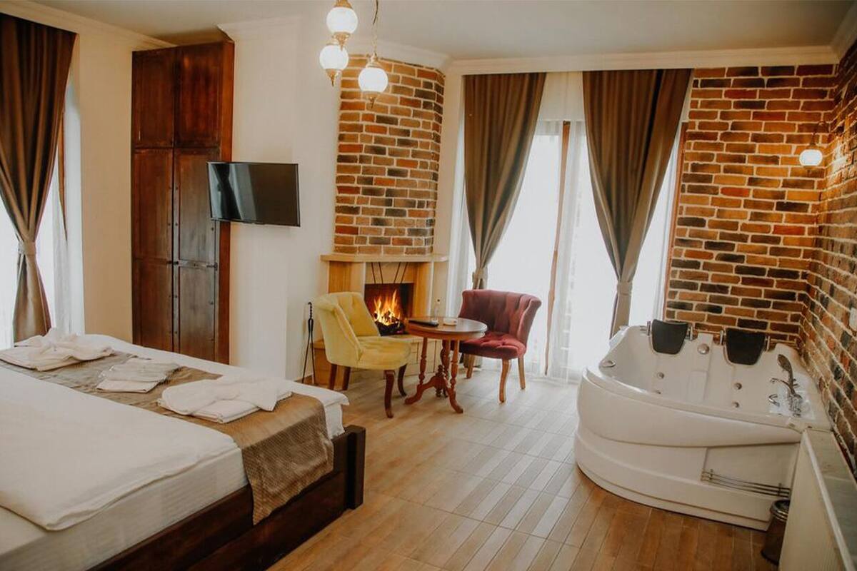 Habitación de hotel con pared de ladrillo, chimenea, cama, sofá, mesa y jacuzzi.