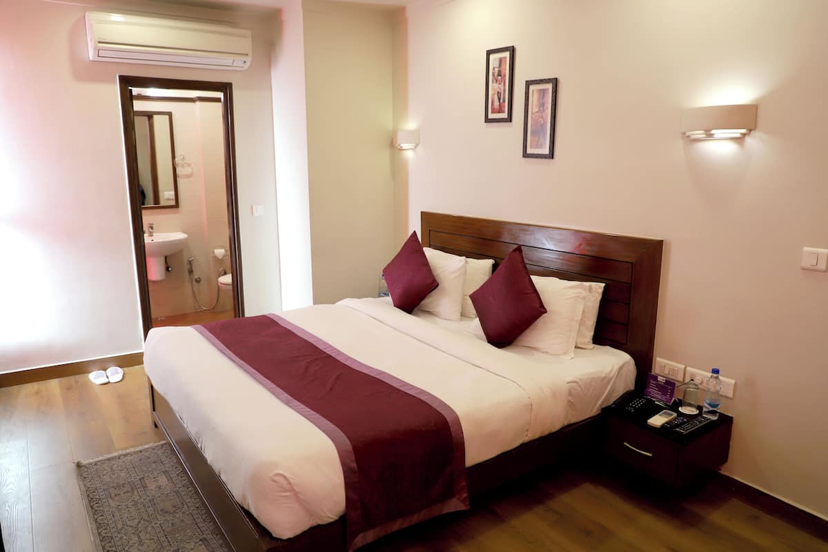 Una cama bien hecha con cabecera de madera, una mesita de noche con lámpara y un aire acondicionado instalado en la pared.