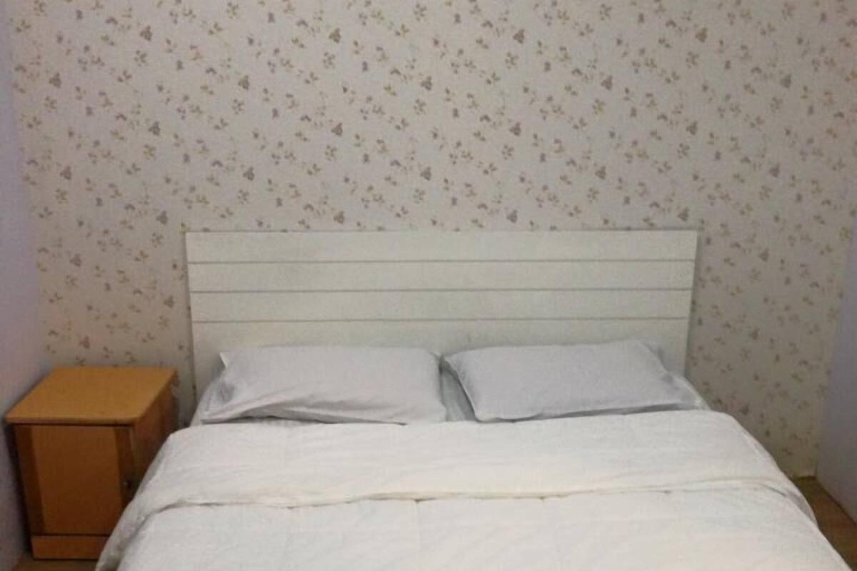 Un lit avec une literie blanche et une tête de lit en bois, dans une pièce dont le papier peint est à motifs floraux.