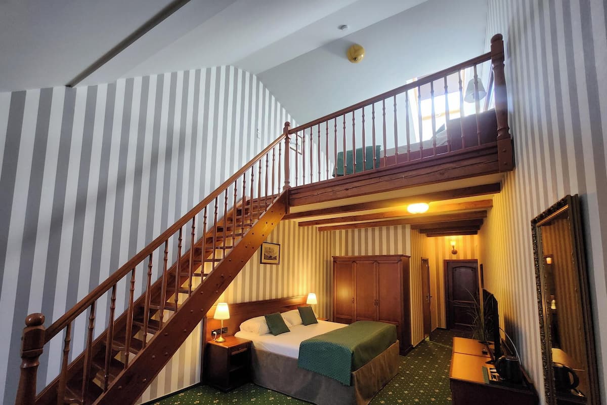 Een kamer met een houten trap, een bed met kussens, een nachtkastje, een spiegel en een deur.