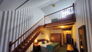 A room with a wooden staircase, a bed with pillows, a nightstand, a mirror, and a door.