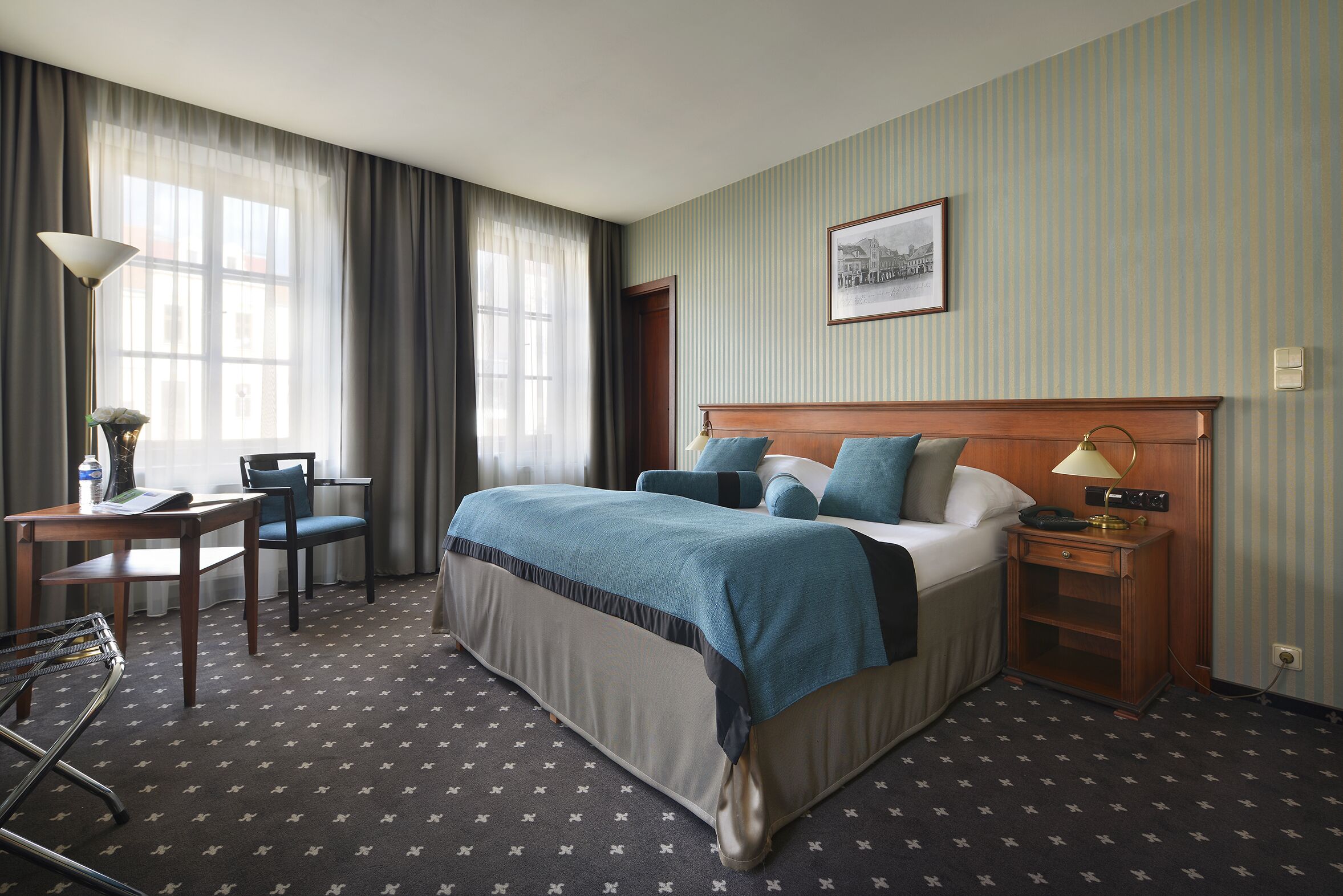 A hotel room with a large bed, a desk with a chair, a lamp, and a framed picture on the wall.