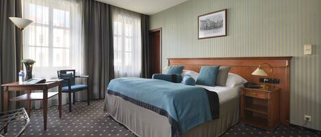 A hotel room with a large bed, a desk with a chair, a lamp, and a framed picture on the wall.