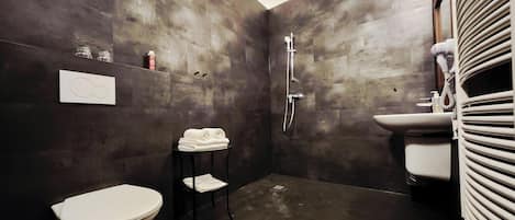 A bathroom with a toilet, a shower, a sink, and a towel rack.