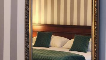 Ein Zimmer mit einem Bett, einem Kopfteil, einem gerahmten Bild an der Wand und einem Spiegel mit aufwendiger Rahmenornierung.