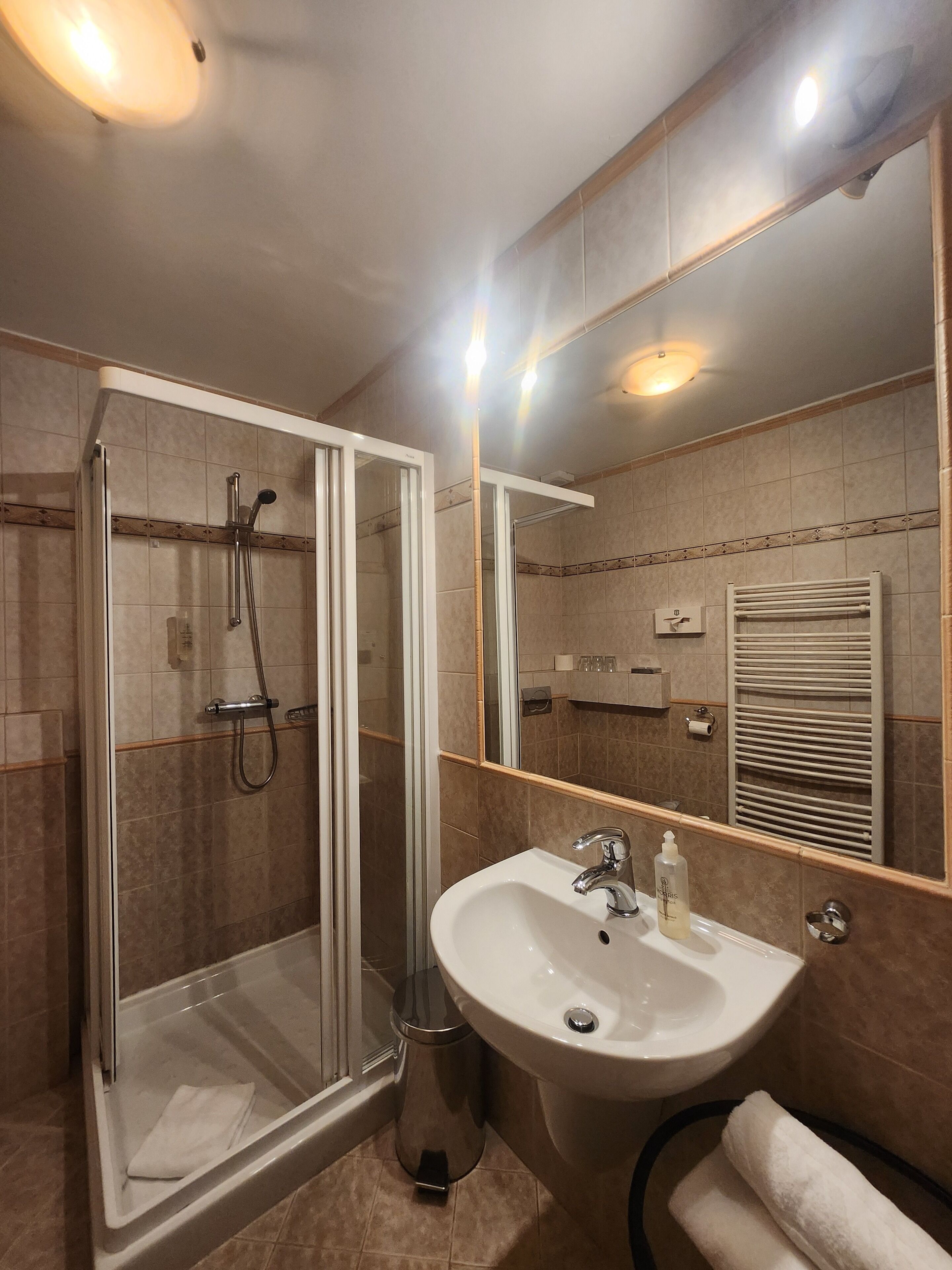 Un bagno con doccia vetro, lavandino, specchio e portasciugamani.
