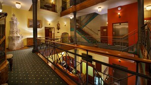 Ein mehrgeschossiges Interieur mit einer Treppe, hölzernen Geländern und einer Statue.