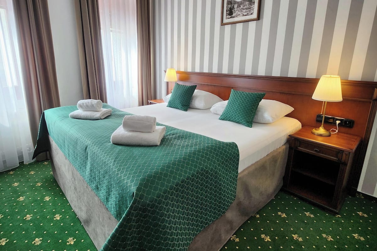 Een hotelkamer met een groot bed, groen beddengoed, een houten hoofdbord, twee bedlampen, een nachtkastje en een gestreept behang.