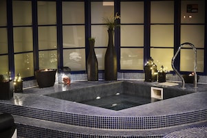 Área de spa com hidromassagem, vasos decorativos e parede revestida de azulejos.