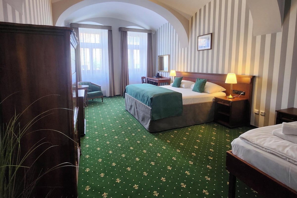 Een hotelkamer met een groen bloemen tapijt, een bed met een groene dekbedovertrek, een bureau met een lamp en een kledingkast.