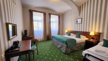 A hotel room with two beds, a desk, a chair, a TV, and a lamp.