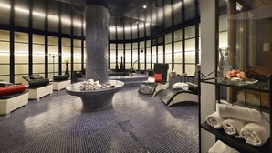 Ein moderner Wellnessbereich mit einer zentralen Whirlwanne, Sitzgelegenheiten und einer Glastheke mit Handtüchern.
