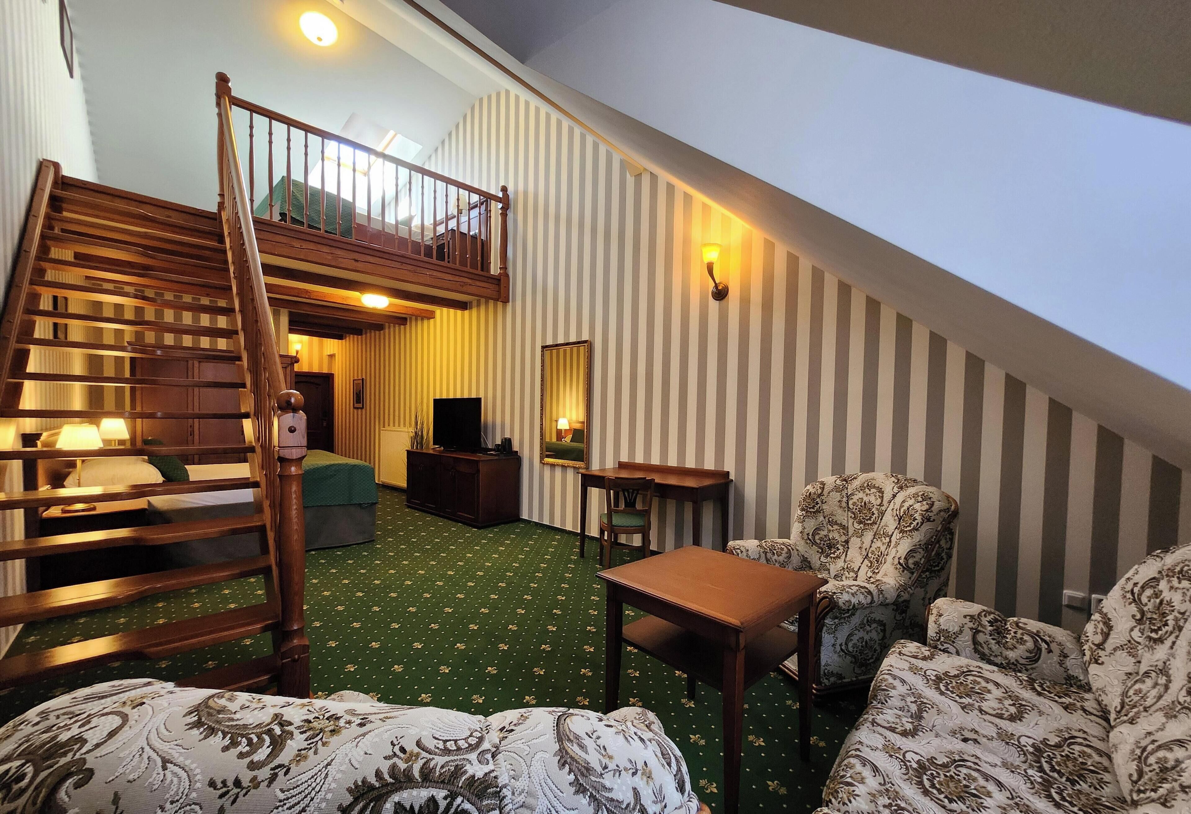 A loft-style room with a wooden staircase, patterned furniture, a small table, and a green carpet.