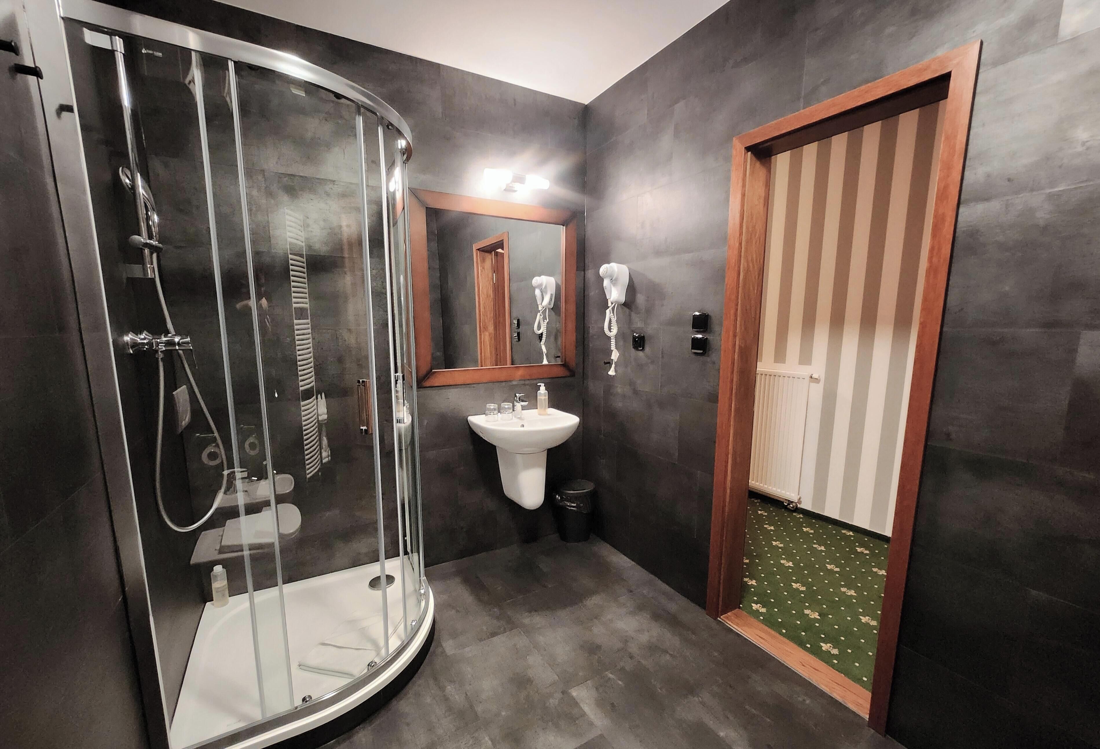 A modern bathroom with a glass-enclosed shower, a pedestal sink, and a wooden-framed door.