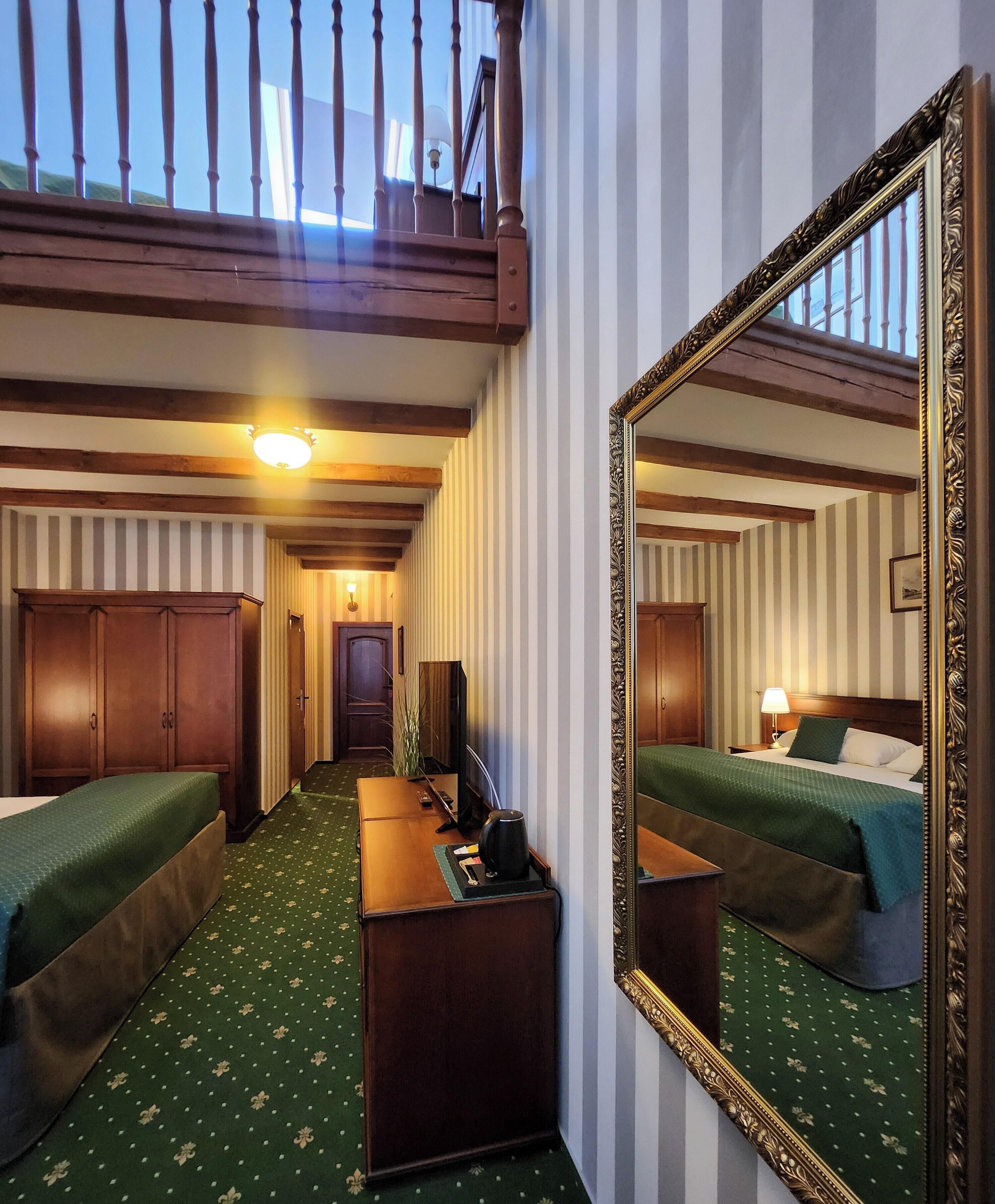 A hotel room with two beds, a desk, a mirror, and a staircase leading to an upper level.