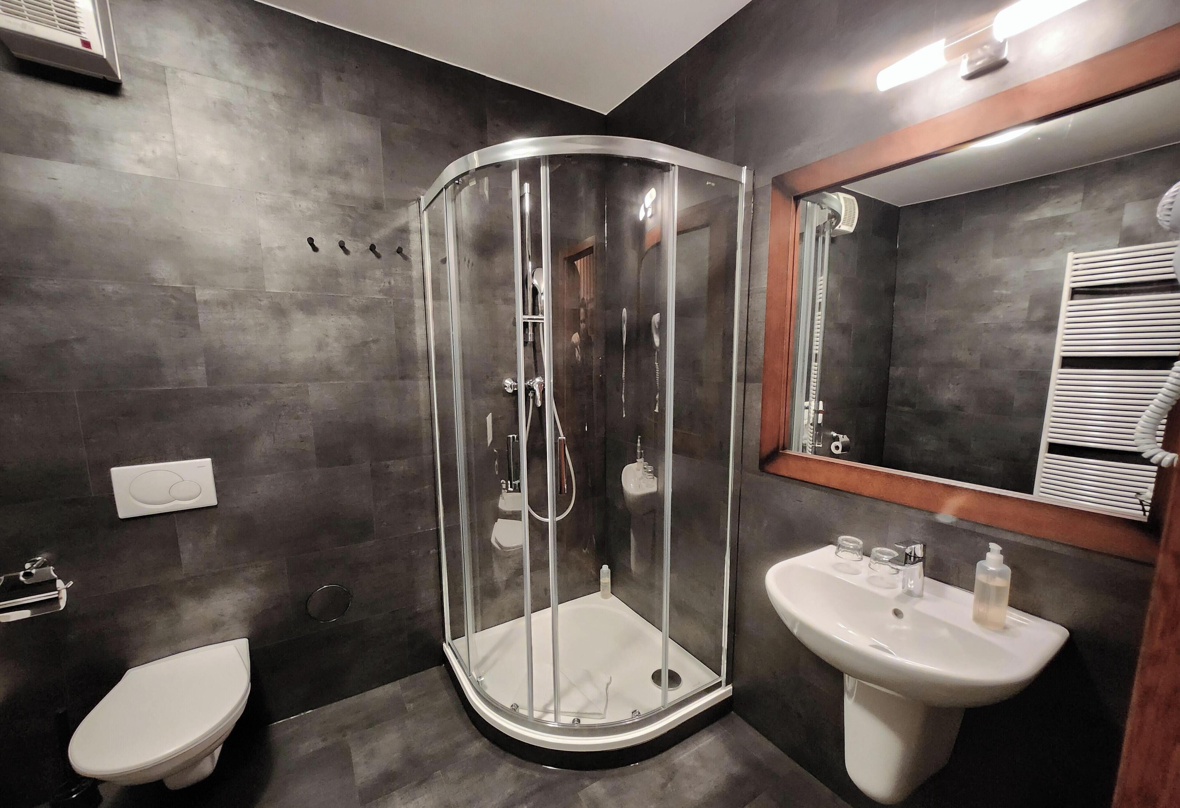 Un baño moderno con ducha acristalada, inodoro blanco y lavabo con artículos de aseo.