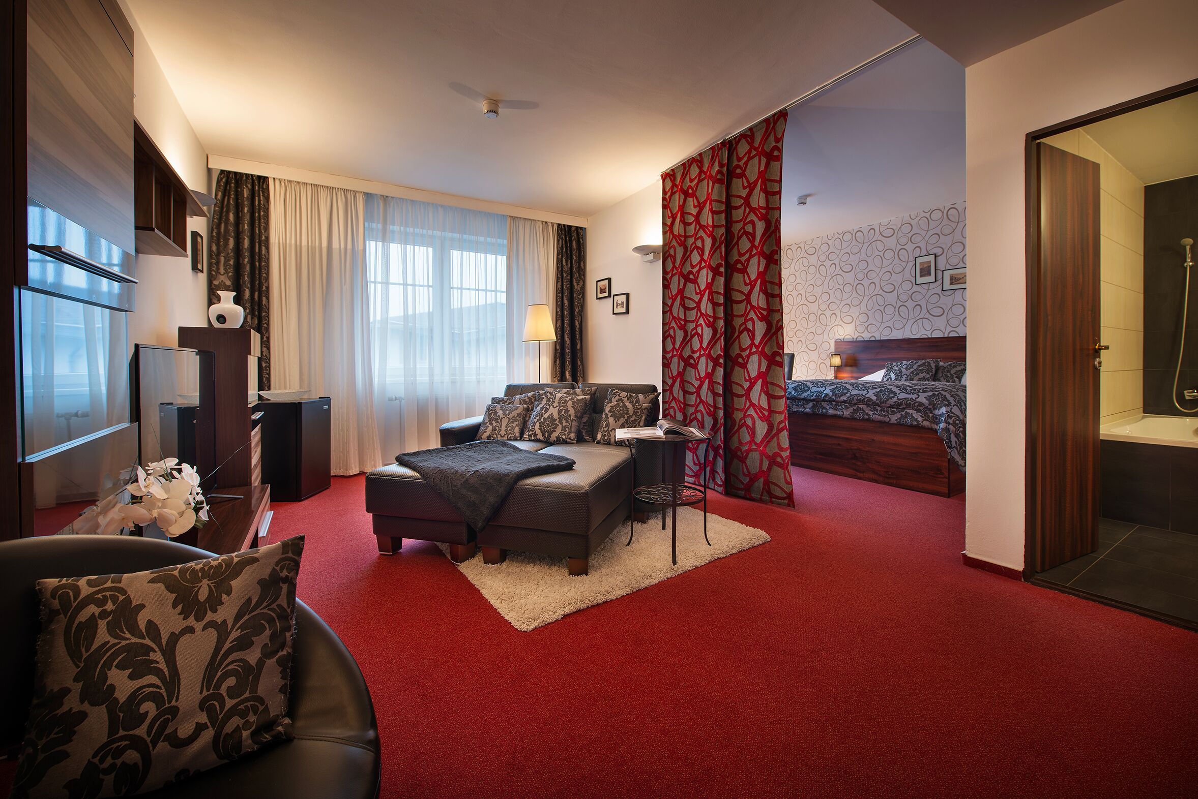 A hotel room with a bed, a sofa, a desk, and a red carpet.