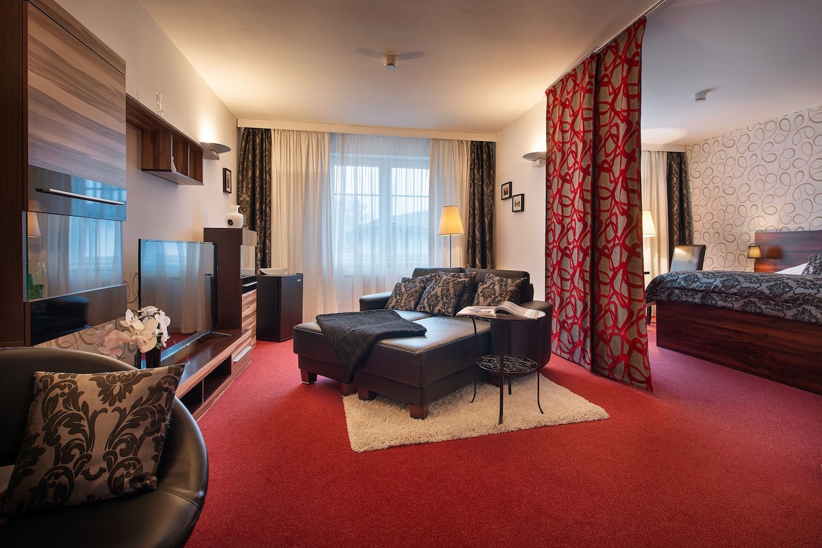 Quarto de hotel com cama, sofá, televisão e escrivaninha.