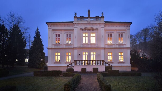 A large, two-story building with a central staircase and multiple windows, surrounded by well-maintained hedges and trees. - Parkhotel Morris Nový Bor (Novy Bor)