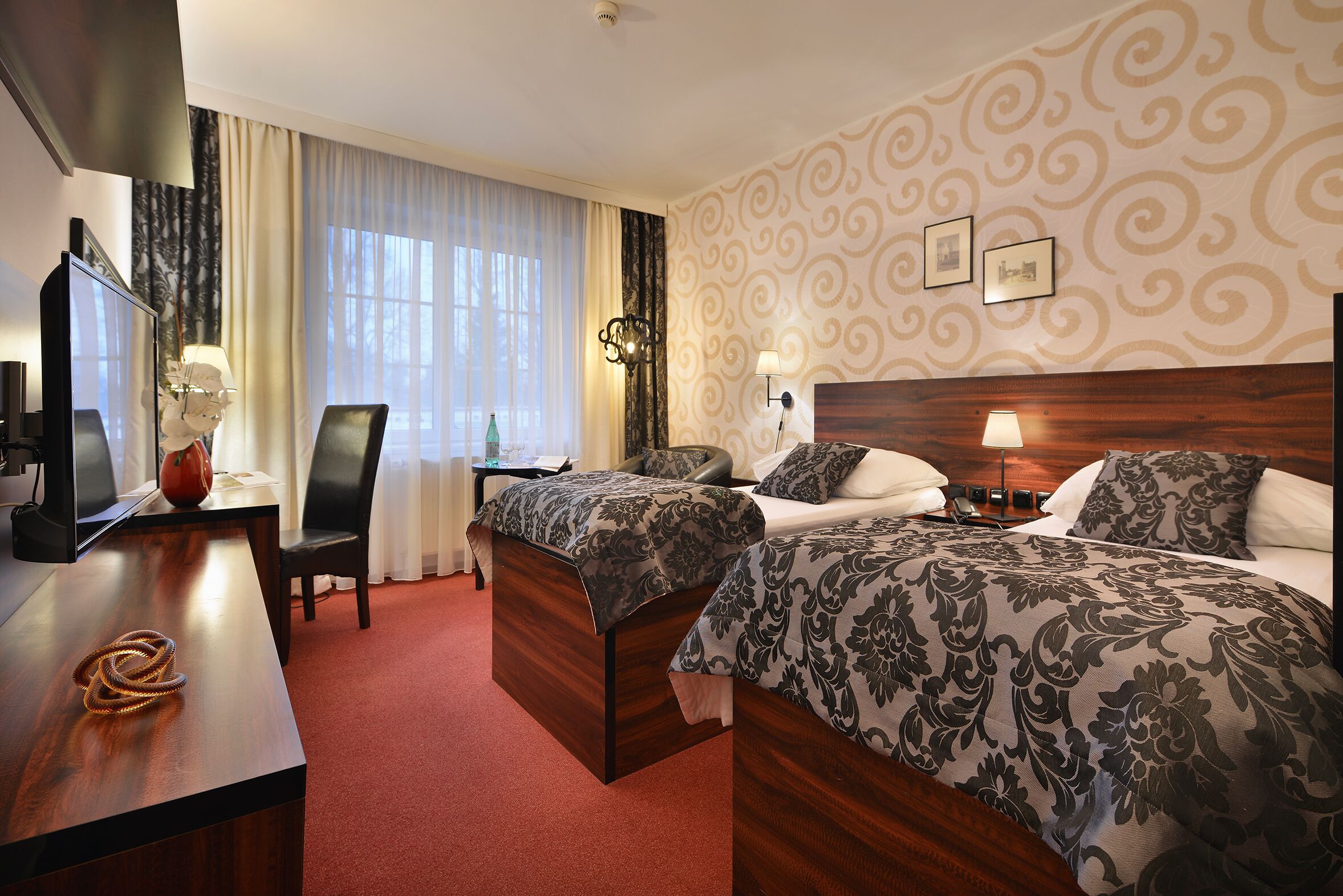A hotel room with two beds, a desk with a TV, and a chair.