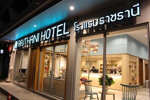 A hotel entrance with a reception desk, chairs, and a display of flowers.