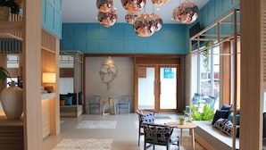 Un hall d’hôtel moderne avec un mur bleu, des meubles en bois et une grande fenêtre ornée de plantes.